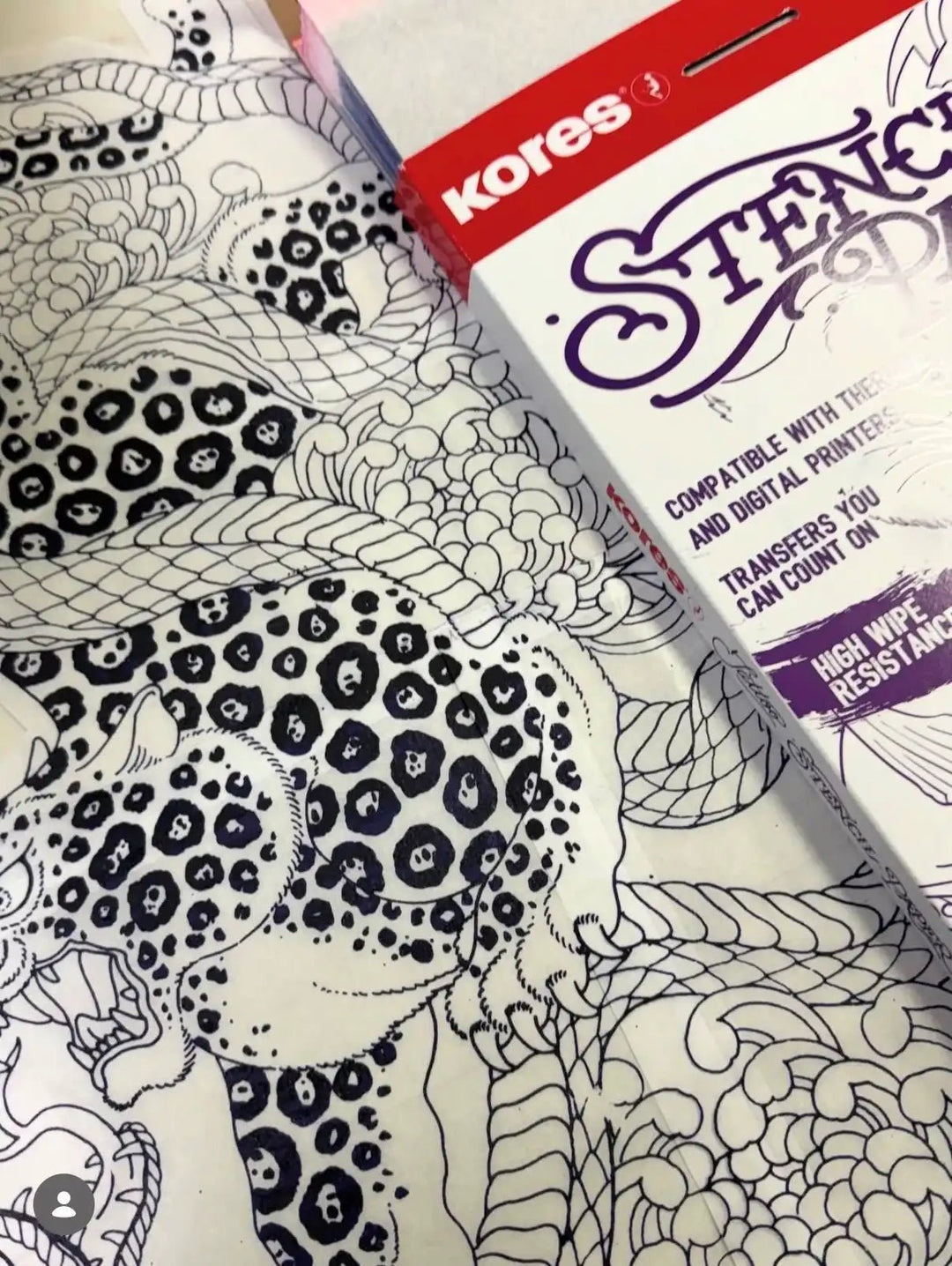 Close-up of a Japanese-style leopard and dragon tattoo stencil linework next to the Kores Carbon &amp; Ribbon stencil paper box.